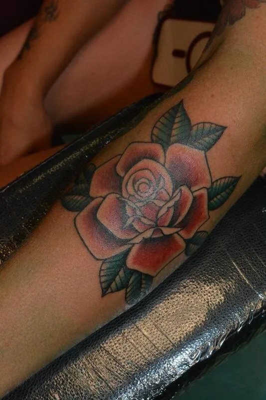 Black and grey Traditional rose tattoo on the forearm with full leaf wrap and soft petal shading, by Scripttoria at Ohana Tattoo, Waikiki, Hawaii.